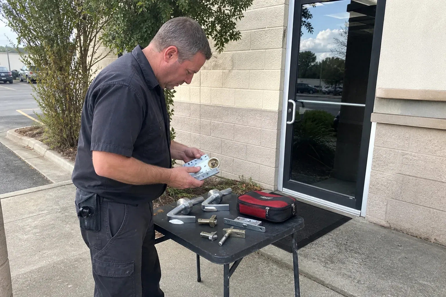 Technician examining detached commercial lock hardware on a table outside a shop entrance. — Business Lockout Service, Peterborough