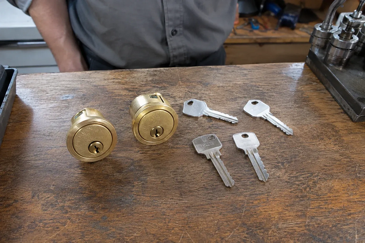 Two detached brass lock cylinders and four house keys on a wooden counter. — Lock Rekeying, Peterborough
