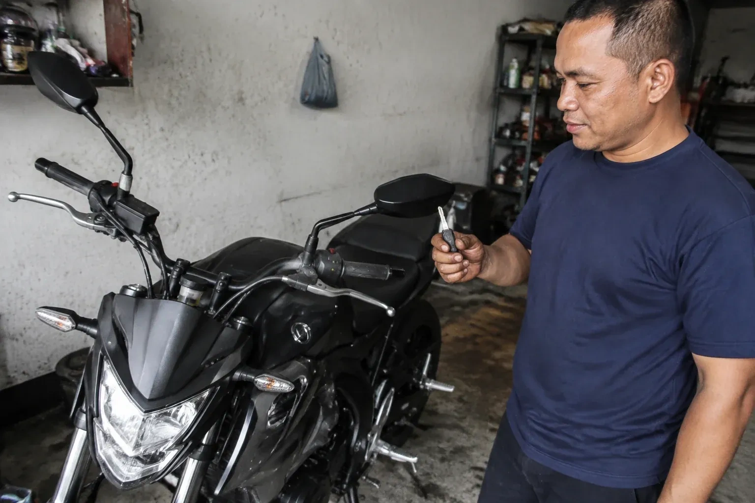 Person holding a key beside a black motorcycle in a garage. — Motorcycle & Scooter Keys, Peterborough