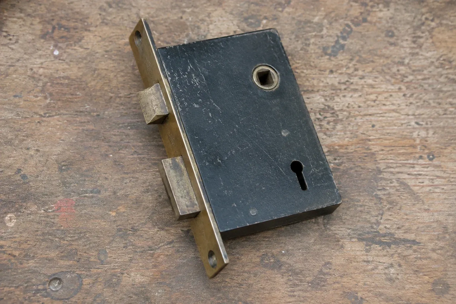 Closed mortise lock case with spindle opening, keyhole, latch and deadbolt on a wooden workbench. — Vintage Mortise Lock Service, Peterborough