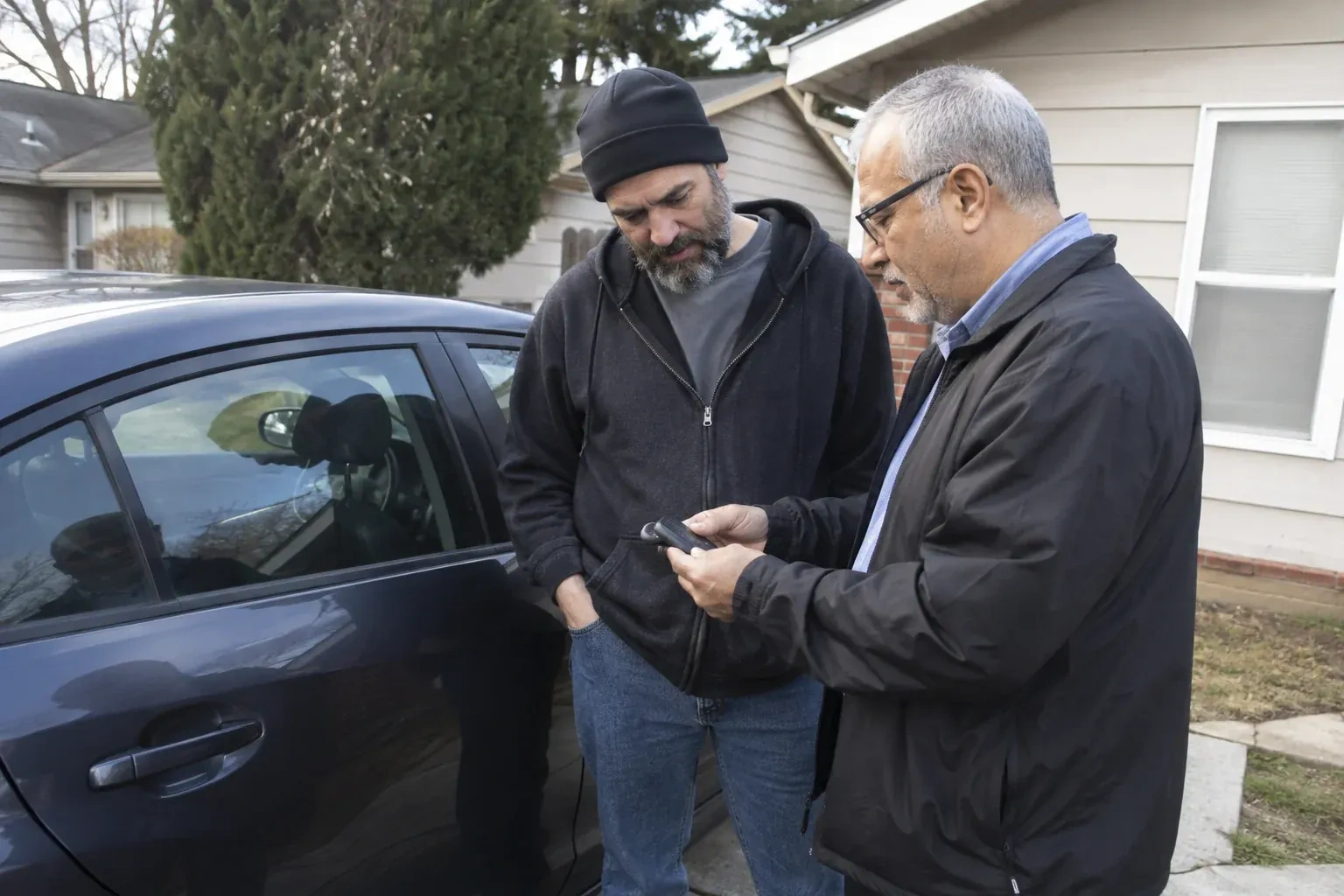 Two adults discussing a key fob beside a parked car. — Car Lockout Service, Peterborough
